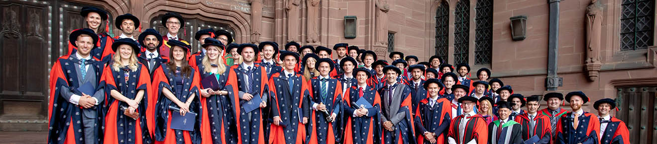 A photo of a large group of people all in graduation robes stood smiling on the steps of the Anglican Cathedral Liverpool